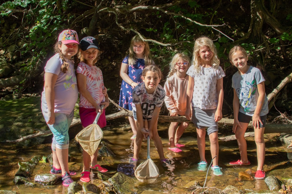 Seven young girls pose with fishing nets while standing in a small creek. 